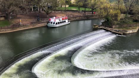 Scenic-View-Of-The-Pulteney-Weir-On-The-River-Avon-In-Bath,-Somerset,-UK-With-Tourist-Boat-Moored-On-The-Side---slow-panning-shot,-aerial