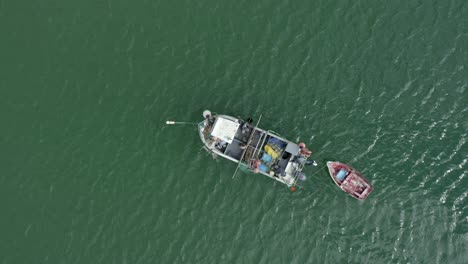 Fischer-Arbeiten-An-Einem-Kleinen-Fischerboot,-Das-Im-Grünen-Wasser-Von-Salema,-Portugal,-Liegt