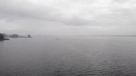 Flying-over-calm-waters-on-a-hazy-morning,-overcast-and-hazy-weather,-a-sailboat-out-on-the-water
