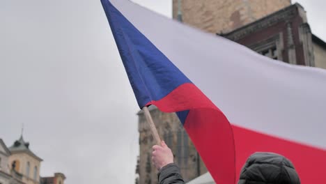 Czech-National-Flag-Waving-in-Hand-of-Male,-Old-Town-Prague-During-Protest,-Slow-Motion-Close-Up
