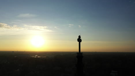 An-aerial-shot-of-a-cathedral's-steeple-with-a-cross-on-top,-taken-at-sunrise