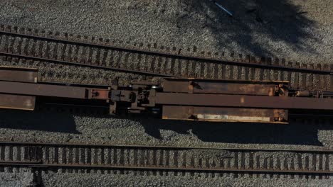 Top-down-view-of-rusty-train-cars-moving-along-a-set-of-tracks-on-a-sunny-day-in-the-morning