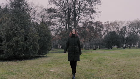 Smiling-confident-woman-walking-towards-the-camera-in-a-park-on-the-green-grass-wearing-black