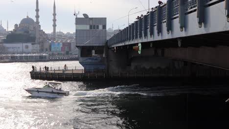 Menschen-Auf-Der-Galata-Brücke-Angeln-Mit-Einem-Schnellboot,-Das-Auf-Dem-Fluss-In-Istanbul,-Türkei,-Unterwegs-Ist