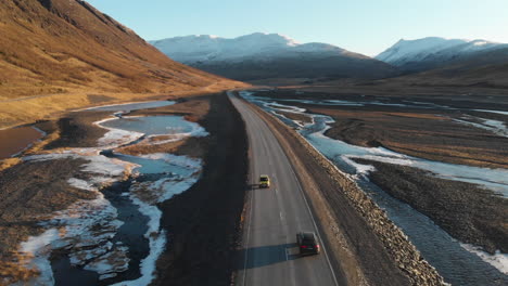 Car-of-Empty-Road-in-Wilderness-of-Iceland-Passing-by-Glacial-Creek-and-Volcanic-Mountains-on-Sunny-Day,-Drone-Aerial-View