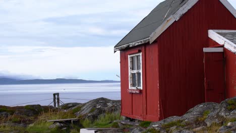 Traditional-Norwegian-red-painted-tiny-wooden-hut-on-the-rocky-beach