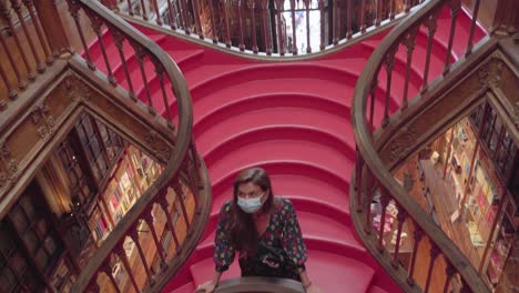 A-woman-stands-on-the-steps-of-the-spiral-stairs-Livraria-Lello-in-Porto,-during-the-COVID-19-pandemic