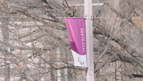 Eine-Feste-Aufnahme-Eines-Banners-Der-Abgesagten-Olympischen-Spiele-2020-In-Tokio,-Das-Mit-Einem-Baum-Im-Hintergrund-In-Tokio,-Japan,-Weht