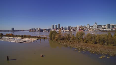 Modern-City-Of-New-Westminster,-British-Columbia,-Canada-Aerial-over-Fraser-River-logging-Quayside-boardwalk-on-a-bright-day-with-blue-sky