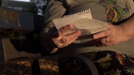 Hands-of-mature-woman-holding-letter-in-the-park-close-up-shot