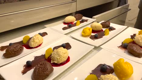 Hand-of-chef-serving-delicious-dessert-with-chocolate-and-vanilla-mousse,-mango-sherbet-and-raspberry-sauce