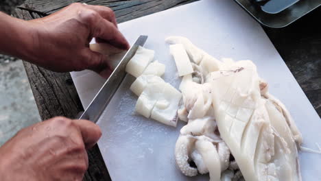 Person-cuts-a-squid-fillet-with-a-knife-into-calamari-rings,-white-cutting-board