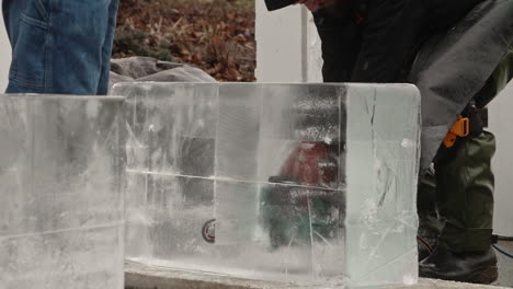 Sculptor-cutting-through-ice-block-with-electric-chainsaw,-Slow-Motion