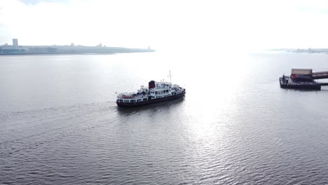 Aerial-view-following-Mersey-commuter-passenger-ferry-in-shimmering-river-arriving-Woodside-terminal-Birkenhead