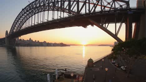Sonnenaufgang-Im-Zeitraffer-Des-Hafens-Von-Sydney-Mit-Booten,-Die-Unter-Der-Brücke-Aufs-Meer-Hinausfahren