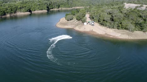 Pull-back-ascending-aerial-view-of-a-jet-ski-turning-circles-on-a-tropical-lake