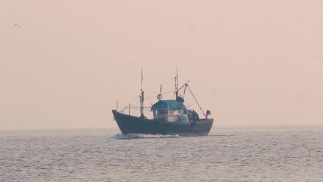 A-Small-fisherman-boat-sailing-in-middle-of-the-ocean-during-sunset-with-small-calm-waves-and-returning-home-in-foggy-weather-video-background-in-mov-in-full-HD