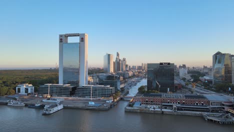 Aerial-dolly-out-of-boats-in-Puerto-Madero-docks-with-high-rise-window-glass-buildings-at-sunset,-Buenos-Aires