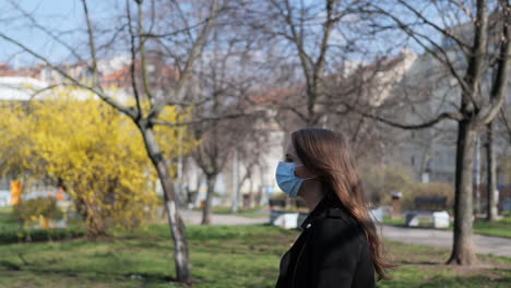 Young-Woman-With-Protective-Face-Mask-During-Covid-19-Virus-Pandemic-Walking-in-Public-Park-on-Sunny-Autumn-Day,-Slow-Motion