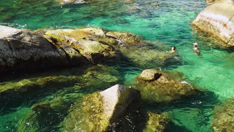 People-swim-in-clear-tropical-sea-among-rocks-of-hidden-secluded-beach