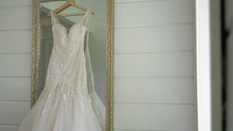 Elegant-wedding-gown-hanging-in-a-mirror-in-a-clean-well-lit-white-room-at-Le-Belvédère-in-Wakefield,-Quebec,-Canada