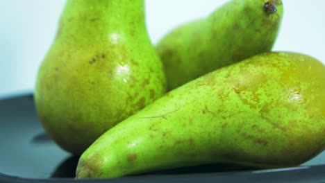 Fresh-big-green-pears-rotates-slowly-on-a-black-plate-on-light-blue-background,-healthy-food-concept,-extreme-close-up-shot,-camera-rotate-left