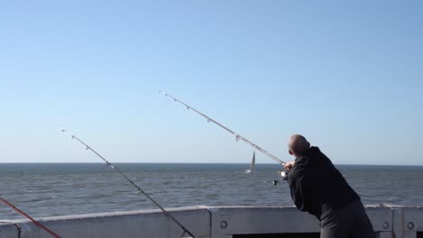 Caucasian-Fishermen-Throwing-Fishing-Rod-Into-North-Sea-during-blue-sky-and-sunlight