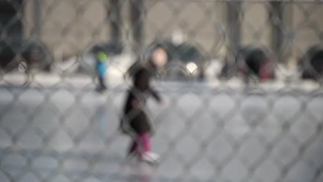 Abstract-shot-of-people-skating-at-an-outdoor-ice-rink-through-a-chain-link-fence