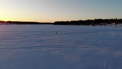 Man-controlling-the-drone-in-the-middle-of-the-Ice-river-lake-to-see-the-sunset-in-Rovaniemi