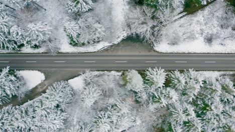 Aerial-tracking-of-a-red-car-which-is-driving-through-a-wintry-countryside-street,-straight-from-above-filmed-drone-footage