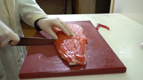 White-coated-fish-industry-worker-cutting-a-salmon-filet-in-two-pieces---slow-motion-static-shot-from-the-side