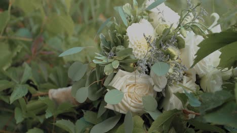 Die-Braut-Pflückt-Ihren-Wunderschönen-Blumenstrauß-Aus-Weißen-Rosen-Und-Lilien-Von-Einer-Pflanzenhecke-Im-Hinterhof