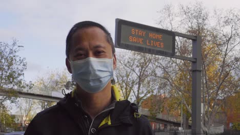 A-sign-reads-'Stay-Home,-Save-Lives'-behind-a-man-wearing-a-mask-during-the-coronavirus-outbreak