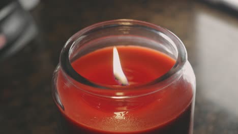 Red-Wax-Candle-In-Glass-With-Wavering-Flame-In-Bokeh-Background