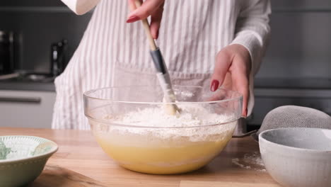 Baker-Mixing-Flour-In-Egg-And-Milk-On-A-Glass-Bowl-Using-A-Silicone-Spatula