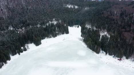 Isolated-frozen-volcanic-crater-lake-in-forest,-Sfanta-Ana,-Romania,-drone-tilt-down