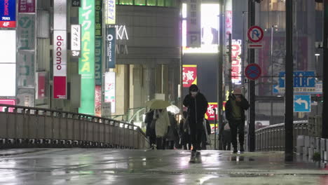 Gente-Con-Mascarilla-Caminando-En-La-Calle-De-Shinjuku-En-Una-Noche-Lluviosa-Durante-Una-Pandemia-En-Tokio,-Japón