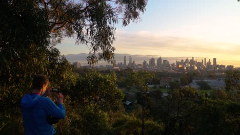 Man-wearing-a-mask-takes-photos-of-a-beautiful-city-skyline-and-sunset