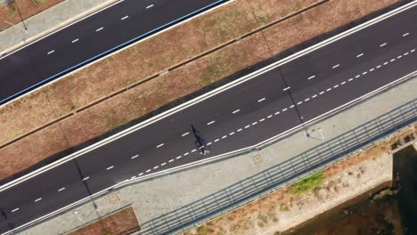 Drone-view-of-a-man-is-riding-bike-on-the-road,-with-shadows