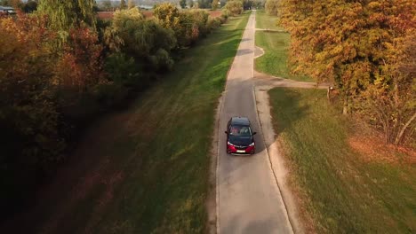 Aerial-view-of-a-black-and-red-Opel-Grandland-car-speeding-on-a-country-road,-at-sunset