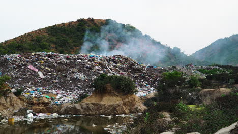 Close-up-of-heap-of-smoking-rubbish-in-an-open-air-dump-in-middle-of-hill-with-sewage