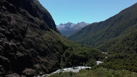 Wild-mountain-river-making-its-way-through-narrow-valley-below-mountain-peaks-in-Fiordland-Southland,-New-Zealand