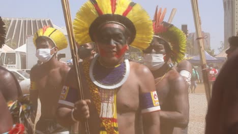 Wearing-traditional-tribal-clothing-from-the-Amazon-rain-forest-and-face-masks-due-to-COVID,-protesters-chant-and-dance-in-Brasilia