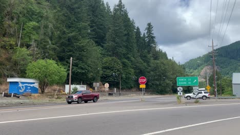 Wide-shot,-cars-drive-by-a-sign-for-Veneta-and-Eugene-in-rural-Oregon
