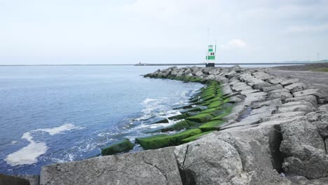 Wave-breaking-rocks-and-lighthouse-on-coastline,-truck-shot