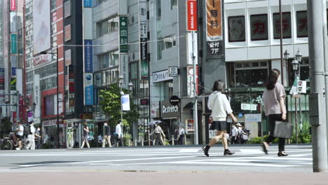 Fußgänger-Und-Radfahrer-Warten,-Bevor-Sie-Eine-Belebte-Straße-In-Tokio-überqueren,-Mit-Sonnenschirmen,-Um-Sich-Vor-Der-Heißen-Sommersonne-Zu-Schützen