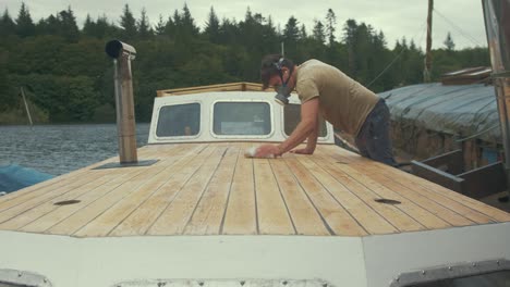 Young-carpenter-wiping-down-sanded-deck-of-wooden-liveaboard-boat