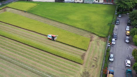 Aerial-drone-footage-Cultivated-rice-paddy-field,-farmer-harvesting-the-crops-with-multifunctional-paddy-harvesting-machine-rice-harvester-tractor-at-Doliu-Yunlin-Taiwan