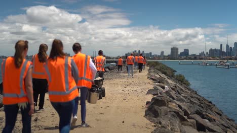 Slow-motion-shot-of-volunteers-cleaning-beach-and-coastline-in-Australia-with-Melbourne-skyline-in-background