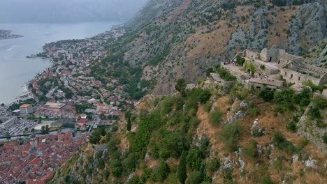 Kotor,-Montenegro-dramatic-left-to-right-aerial-reveal-of-the-old-town-and-harbour-of-luxury-yachts-seen-from-above-the-Ruins-of-Castle-San-Giovanni